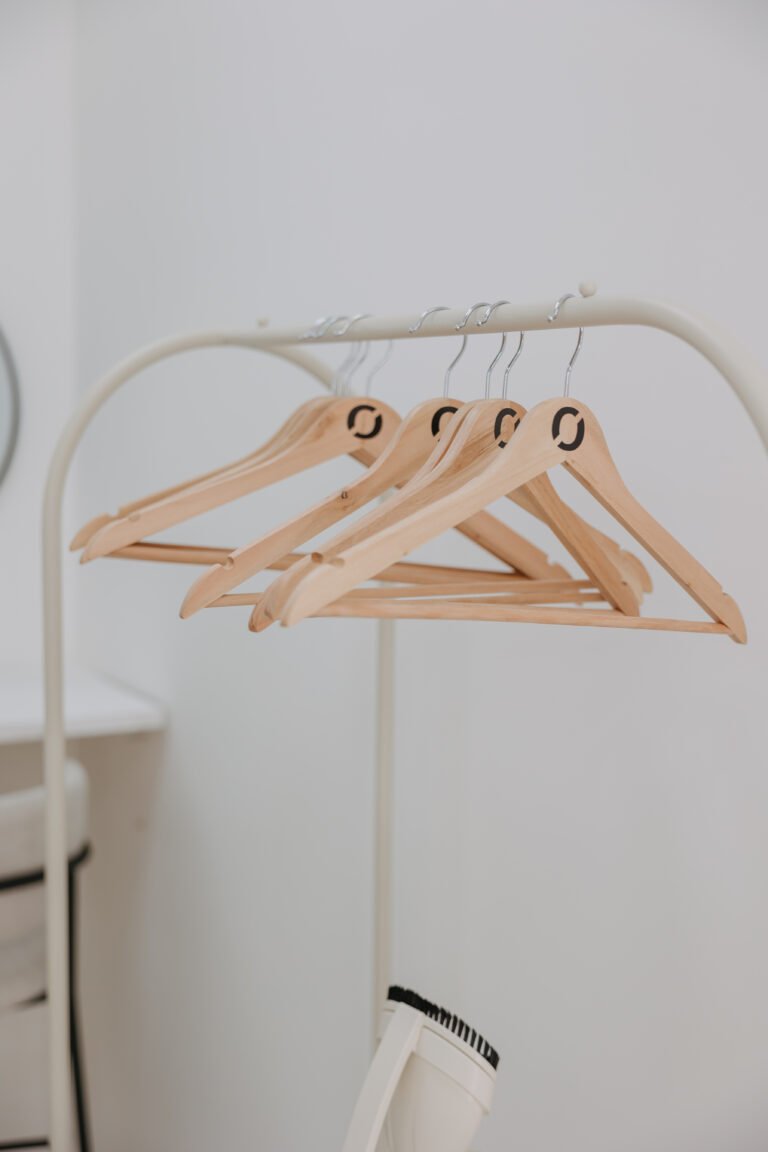 Burro de ropa con perchas de madera sobre pared blanca