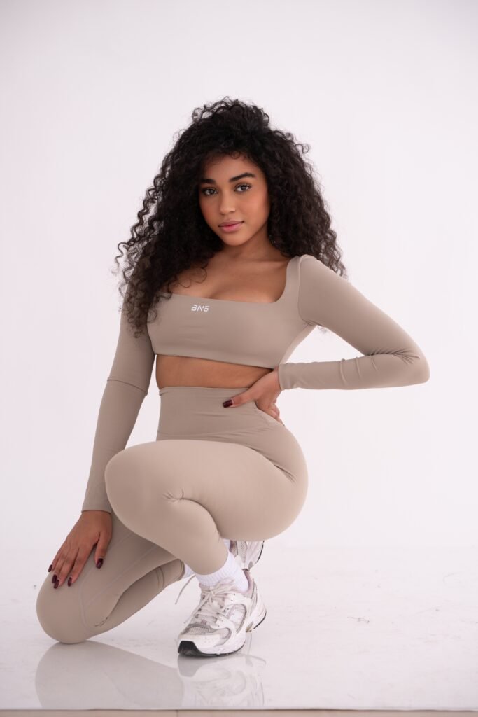 Modelo con conjunto deportivo beige agachada sobre fondo claro