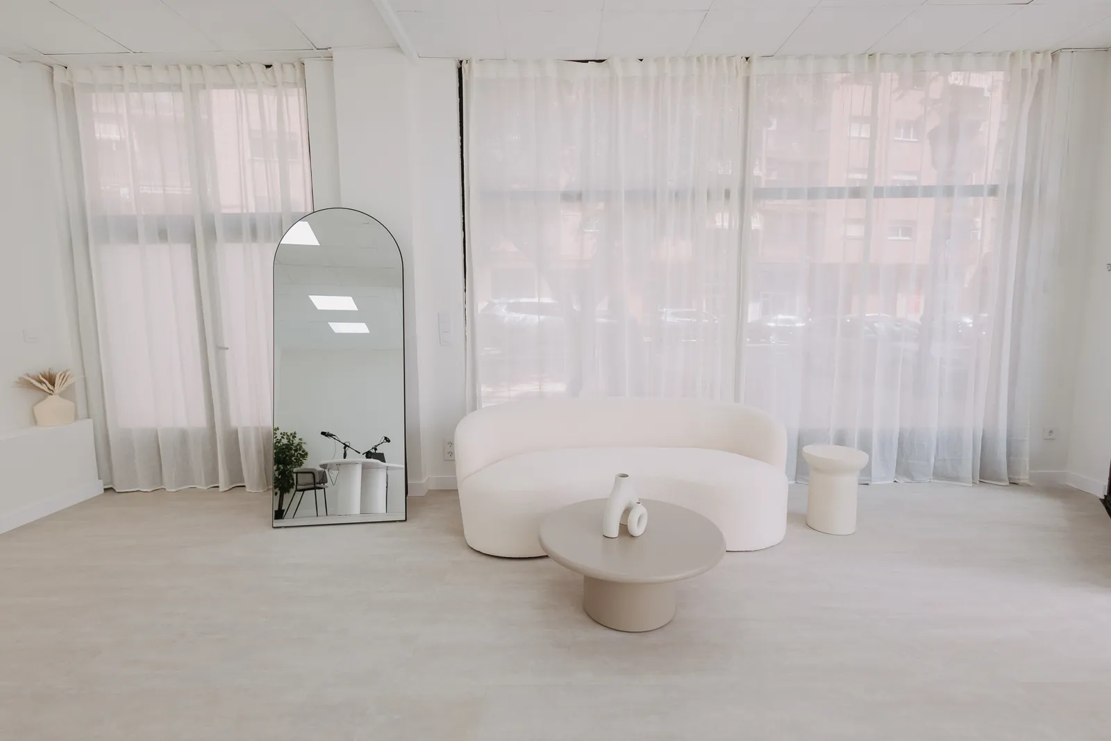 Sala principal del estudio con sofá curvo, espejo de arco y luz natural