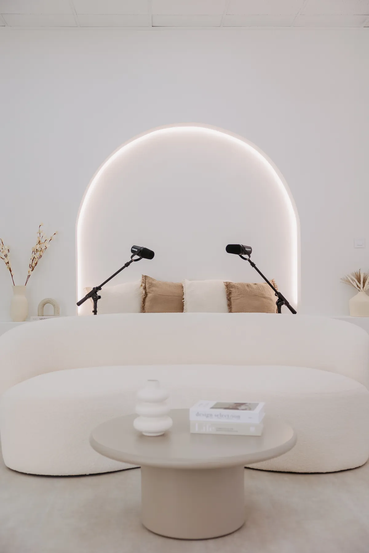 Set de podcast con sofá curvo y micrófonos bajo el arco iluminado